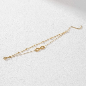 Minimalist double-layer infinity bracelet in gold finish on a white stone background