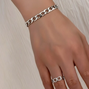 Polished silver cuban chain bracelet and ring set worn on a textured white fabric background