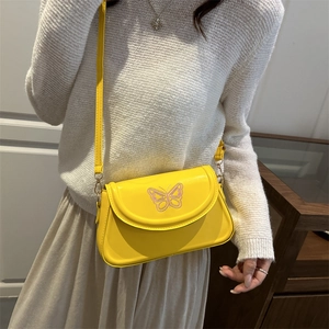 Sac à bandoulière jaune avec broderie papillon porté par un mannequin en décor naturel