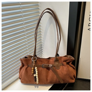 Macro shot of brown suede tote bag featuring metallic buckle and beaded tassel detail