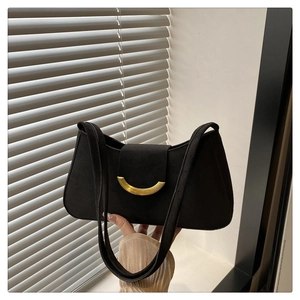 Detail of black suede shoulder bag featuring a prominent gold crescent metal buckle