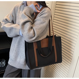 Detail of a large canvas tote bag with brown leather handles worn over the shoulder