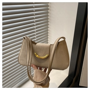 Detailed macro view of beige suede underarm bag featuring a vintage curved gold buckle