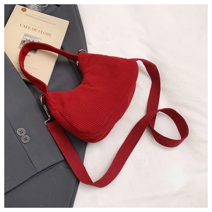 Detail of red corduroy crescent bag showing wide strap and metallic hardware accents