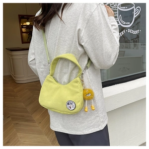 Street view of a light green corduroy tote bag with embroidery and a plush toy charm