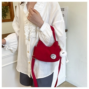 Detail of red corduroy shoulder bag featuring a cute cartoon badge and plush pompom charm