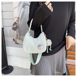 Detail of light green corduroy hobo bag with cartoon badge and soft pom-pom pendant