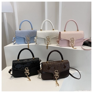 Detail view of five luxury faux snake skin handbags with gold logo and tassel on white podium