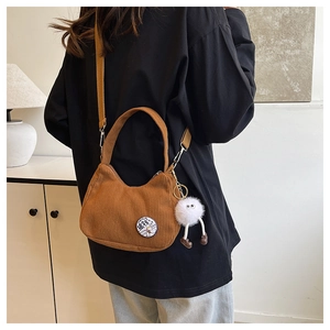 Rear view of a brown corduroy crossbody bag with pom-pom charm and cartoon patch detail