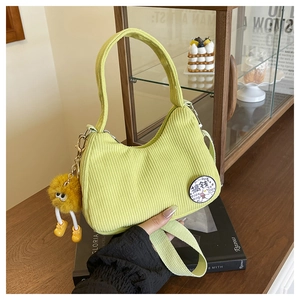 Detail of light green corduroy shoulder bag featuring cartoon embroidery and plush pendant