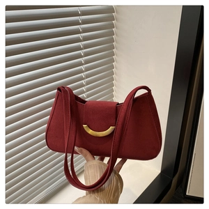 Detail of burgundy suede shoulder bag with a gold crescent buckle and smooth leather texture