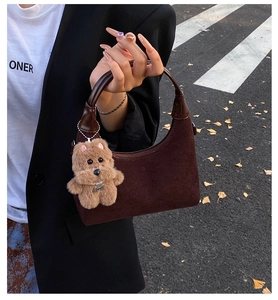 Detail of dark brown suede crescent bag with a cute plush dog charm on an autumn street