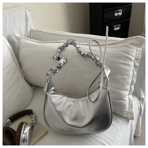 Detailed view of silver hobo bag with pleated scrunchie strap on white sofa decor