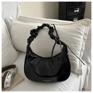 Detail of glossy black patent leather dumpling bag with pleated handle and fashion text