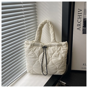 Detail of cream quilted tote bag showing heart stitching and black drawstring closure