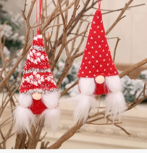 Detail of two red knitted Christmas gnome ornaments hanging on a rustic tree branch