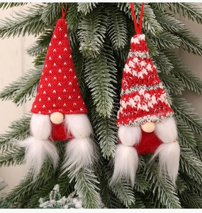 Detail of two knitted Christmas gnomes with long white beards hanging on a green pine tree