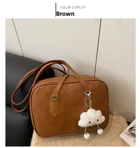 Detail view of brown faux leather Boston bag with a white plush cloud charm accessory