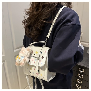 Detail of cream crossbody bag with colorful graffiti prints and pink plush charm accessory