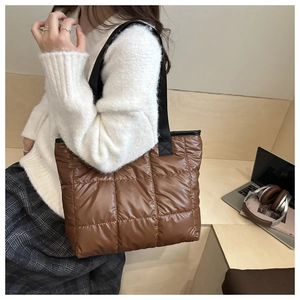 Brown quilted puffer tote bag with black strap shown in a casual lifestyle setting