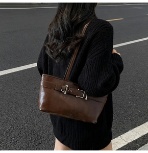 Détail du sac bandoulière en cuir marron foncé avec boucle argentée porté à l'épaule