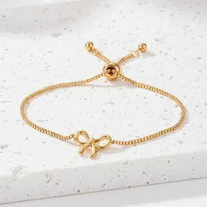 Elegant gold bow pendant bracelet with adjustable box chain on white stone surface