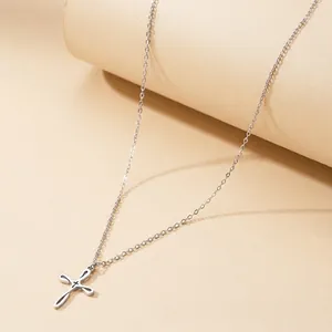 Collier croix minimaliste en acier inoxydable argenté sur un support d'exposition