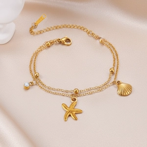 Macro detail of gold-plated starfish and shell charms on a double-layer steel bracelet