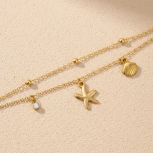 Detail of double-layer gold chain with seashell, starfish charms and zircon pendant