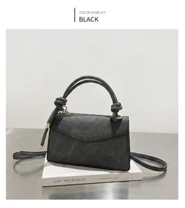 Detail of black textured leather bag with gold knot buckle and removable shoulder strap
