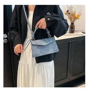 Detail of light blue textured crossbody bag with a unique knot-style handle and flap cover