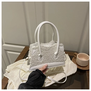 Close-up of white plush crossbody bag with leather trim on a cozy interior setting