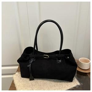 Detail of a black suede tote bag with a golden metal buckle on a cozy wooden desk