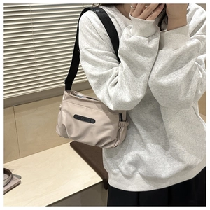 Detail view of adjustable black strap and side pleated pocket on beige nylon crossbody bag