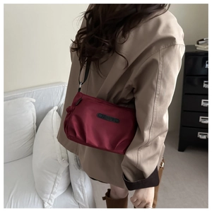 Detailed view of a dark red nylon crossbody bag with black adjustable strap and logo