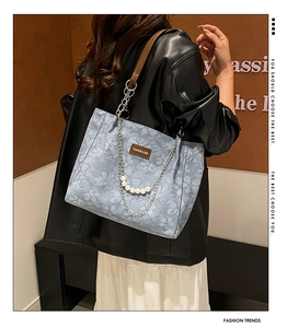 Detail of floral denim tote bag featuring silver chain, pearls, and leather straps