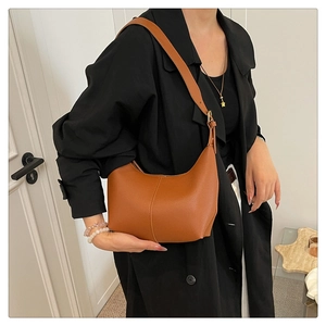 Macro detail of caramel lychee grain leather on a modern hobo shoulder bag with metal buckle