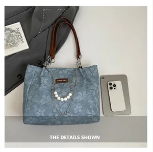 Macro view of blue denim tote bag featuring floral patterns and a pearl chain strap detail