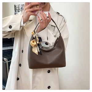 Detail of a brown leather hobo bag with a decorative floral silk scarf on a model