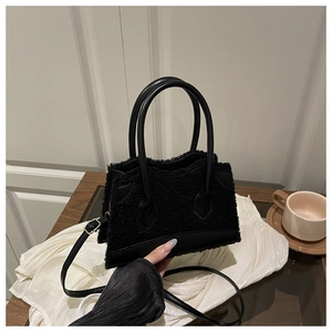 Detail of black faux fur handbag with leather trim and strap on white fabric
