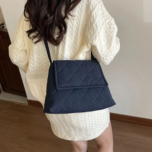 Navy blue quilted crossbody bag with diamond stitch and long strap over white sweater