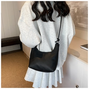 Rear view of a black hobo bag with litchi grain leather on a model's shoulder