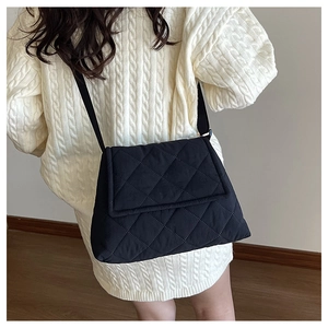 Detail of a black quilted crossbody bag with classic diamond stitching and a fabric strap