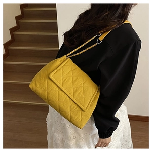 Detail of yellow quilted nylon crossbody bag with chain strap worn by a model on stairs