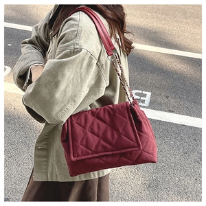 Side view of a burgundy quilted chain crossbody bag worn by a model in natural light