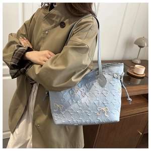 Close-up of light blue quilted tote bag with embroidered bows on a model shoulder