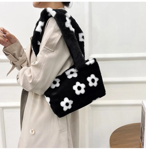 Detail shot of plush black shoulder bag with white flower pattern on a beige coat