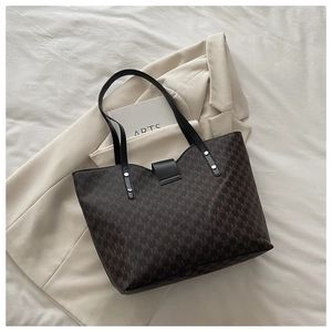 Macro detail of the brown tote bag featuring repeating M patterns and metal rivets