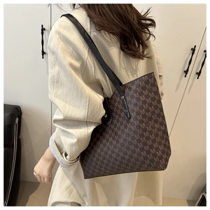 Close-up of a large coffee-brown tote bag with dark M-pattern print and slim black straps
