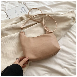 Close-up of beige pebble leather shoulder bag with minimalist crescent shape and thin strap